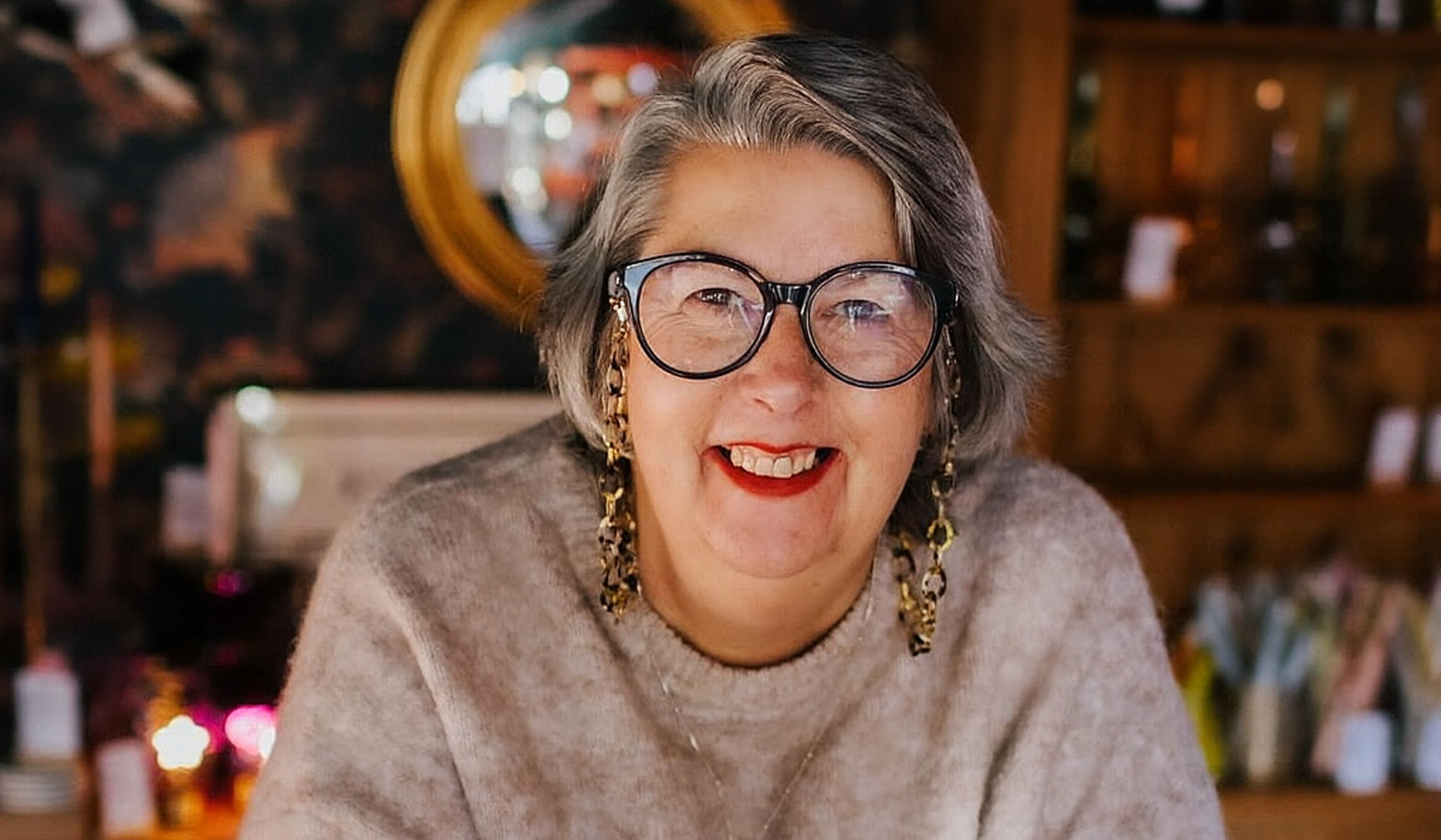 Woman wearing glasses and a beige sweater in a cozy indoor setting