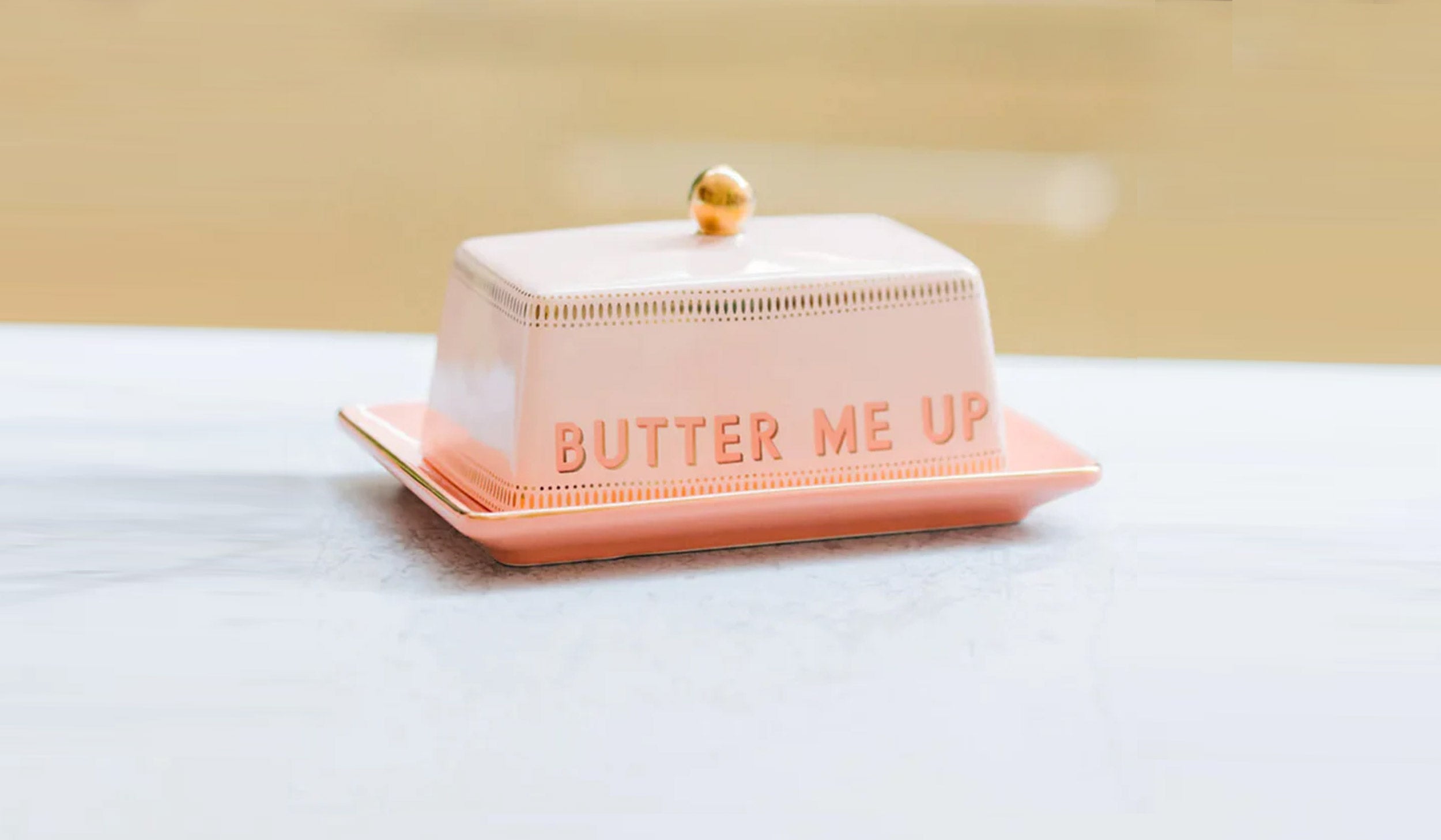Pink butter dish with 'Butter Me Up' text on a white surface
