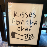 Framed sign with 'Kisses for the chef' text on a wooden surface