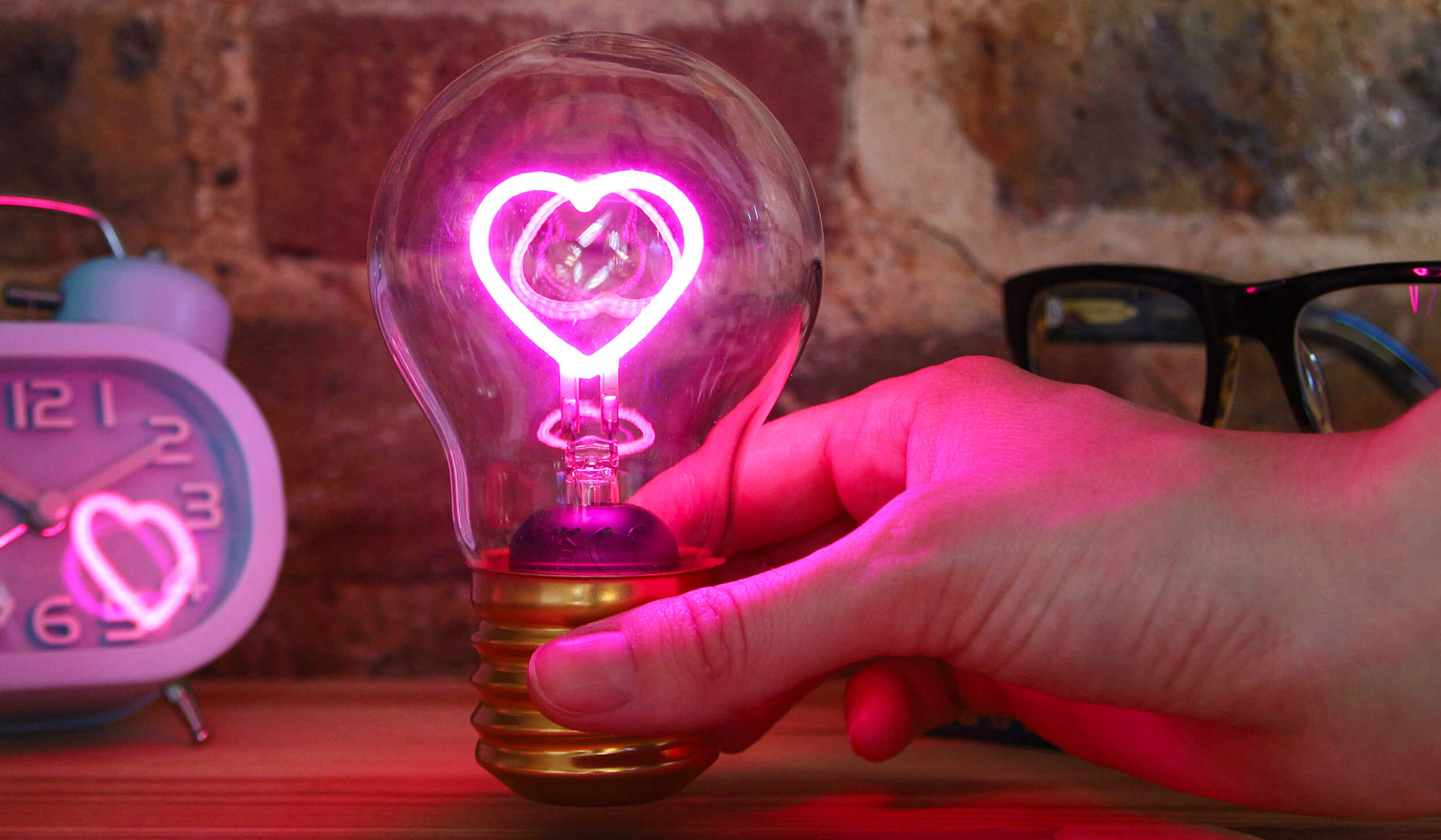 Hand holding a light bulb with a heart design, clock in the background